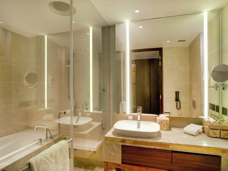 A modern bathroom with a glass-enclosed shower, two sinks, a vanity with a mirror, and a bathtub.