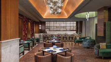 A modern hotel lobby with a bar area, seating arrangements, and a decorative ceiling.