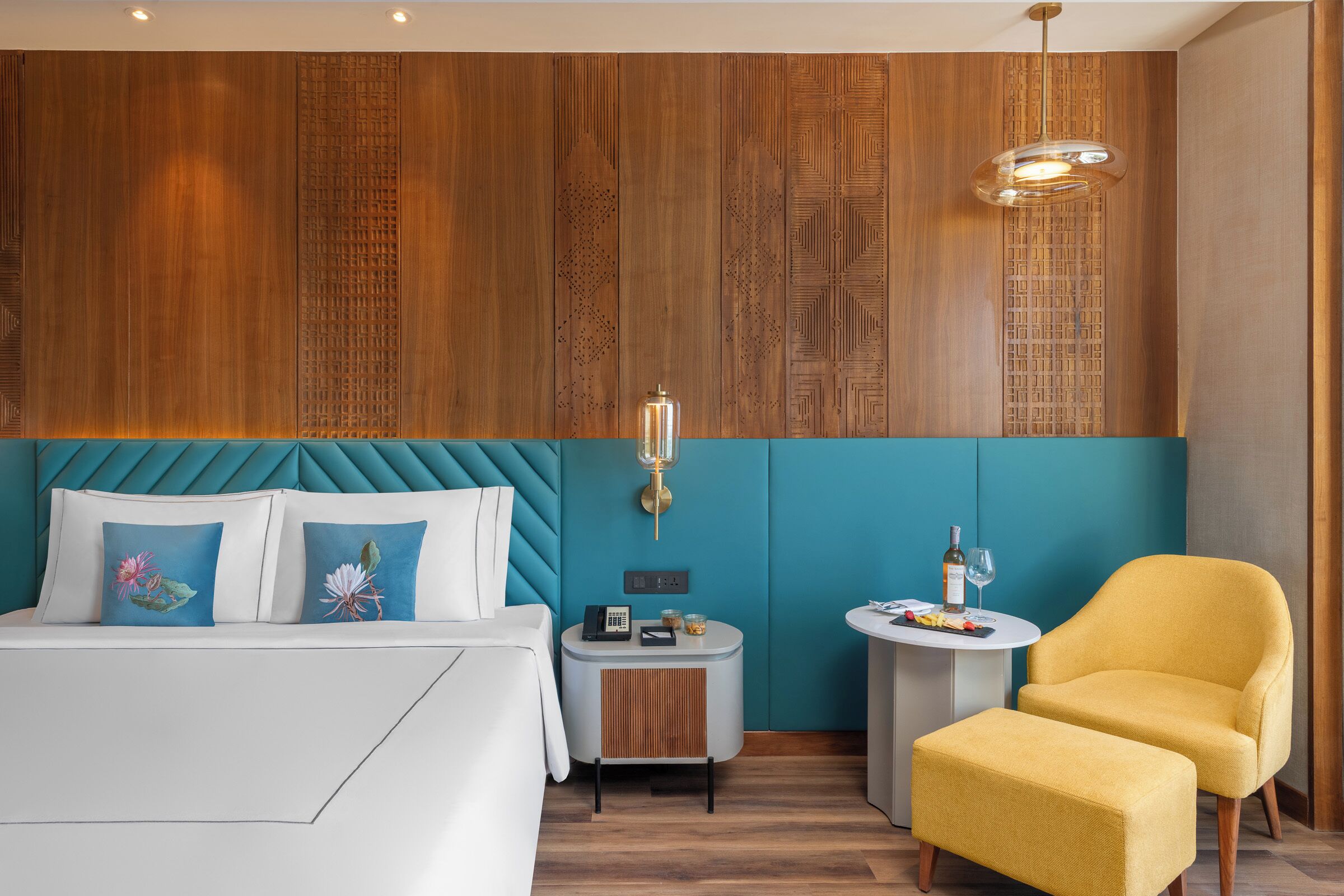 Habitación de hotel con cama, una mesita auxiliar pequeña, una silla y una pared con paneles de madera.