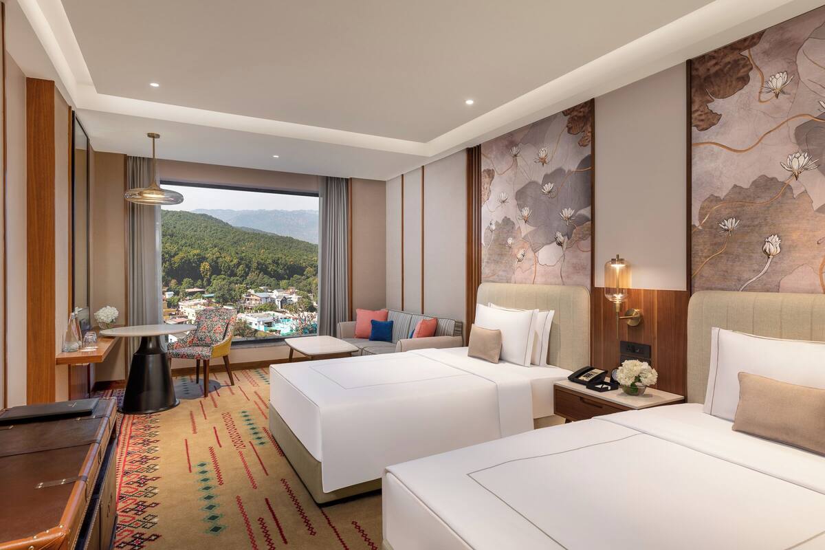Habitación de hotel con dos camas, un escritorio, una silla y vistas a un paisaje montañoso.