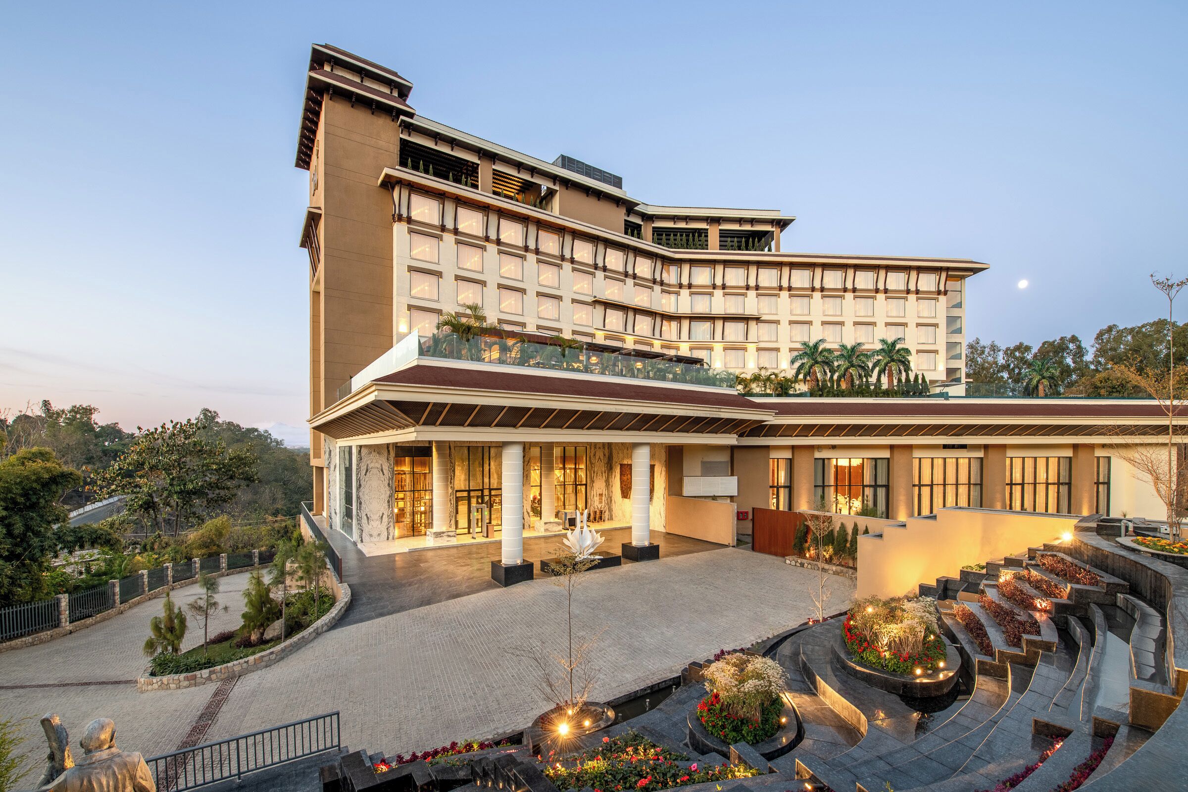 A modern hotel with a curved facade, large windows, and a landscaped courtyard with pathways and plants.