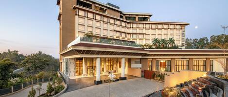 A modern hotel with a curved facade, large windows, and a landscaped courtyard with pathways and plants.