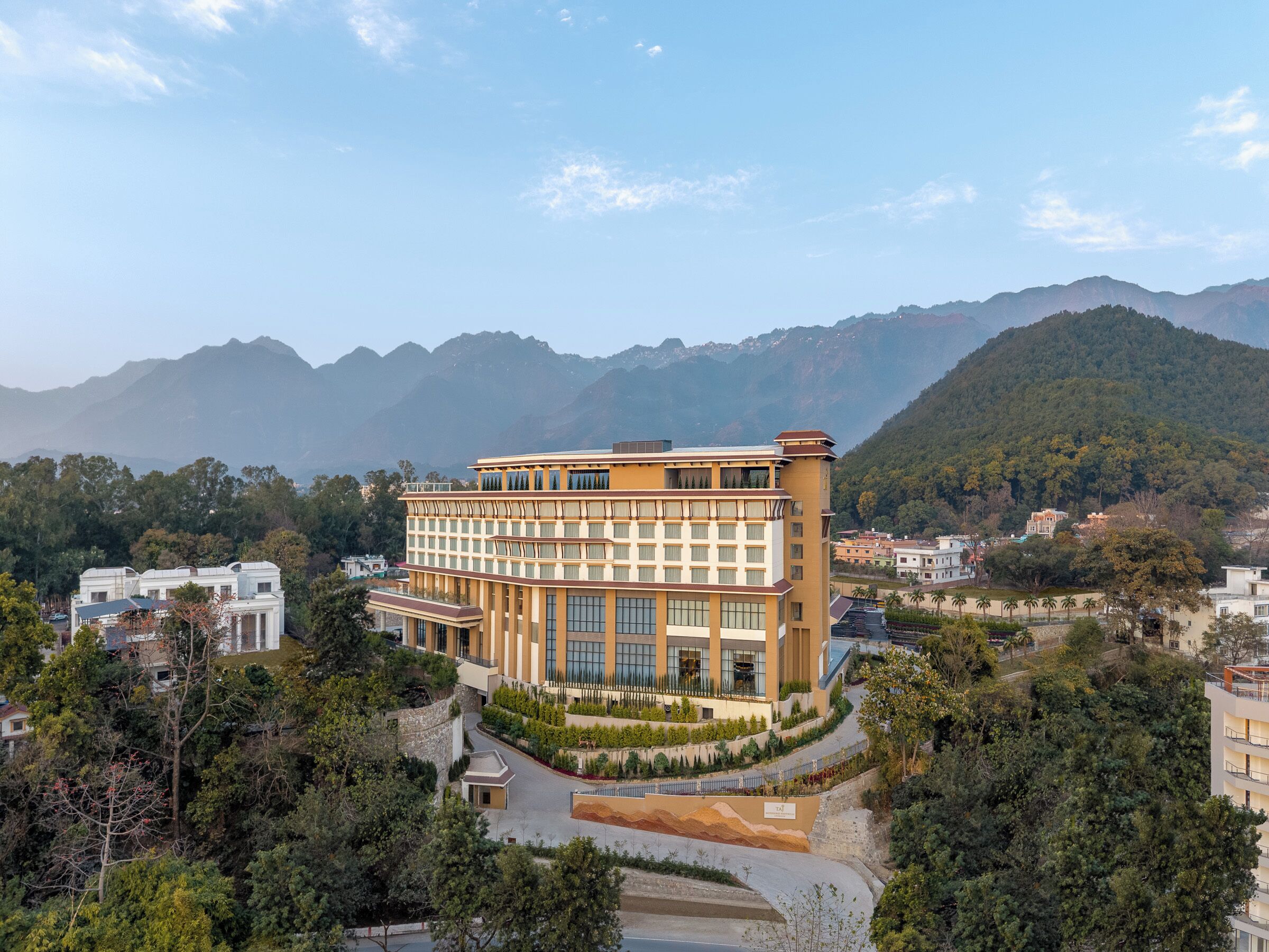 A multi-story hotel with a modern architectural design, surrounded by lush greenery and mountains in the background.