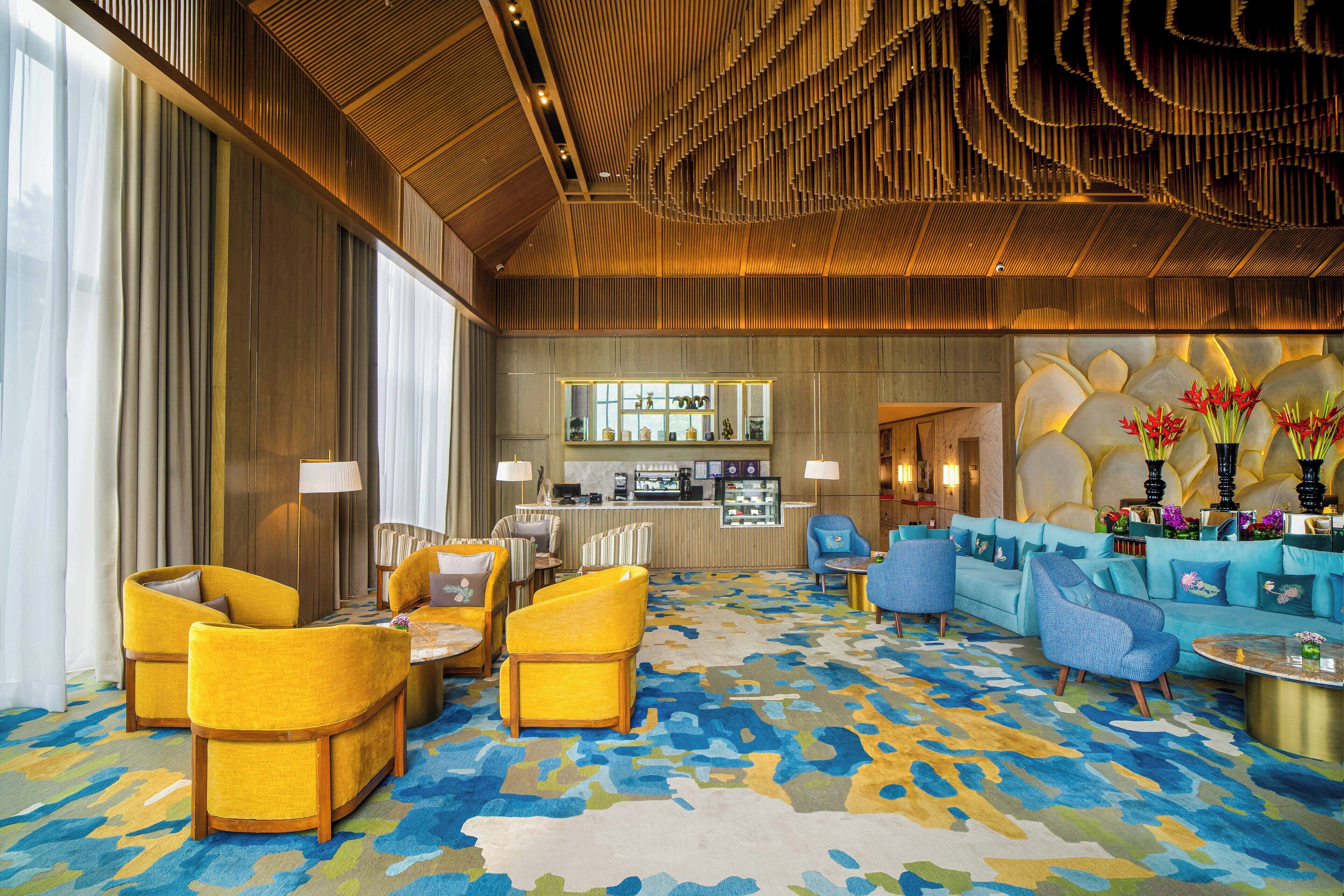 Un hall d’entrée spacieux, doté d’un tapis à motifs, de sièges aux couleurs jaune et bleu, d’un coin bar et d’un plafond décoratif.