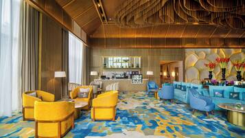 Un hall d’entrée spacieux, doté d’un tapis à motifs, de sièges aux couleurs jaune et bleu, d’un coin bar et d’un plafond décoratif.