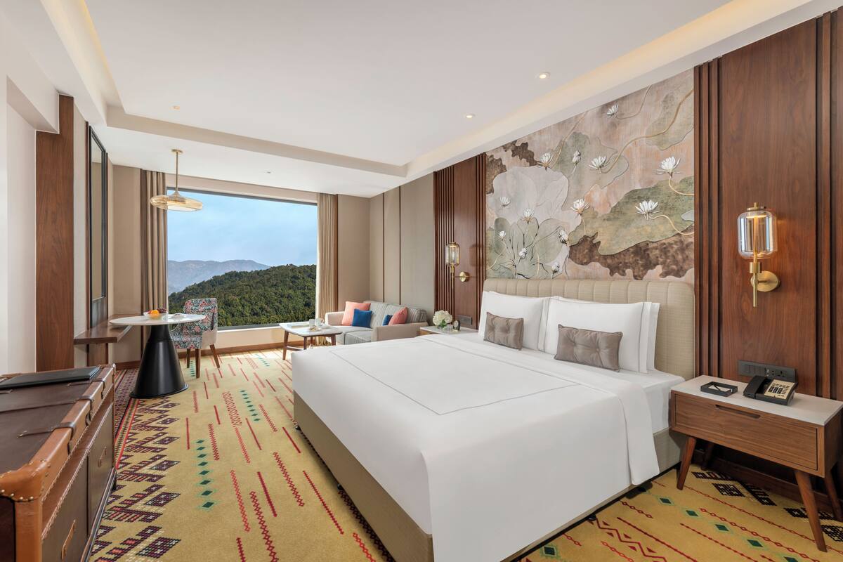 Una habitación de hotel con una cama grande, un escritorio, una silla y vistas a las montañas.
