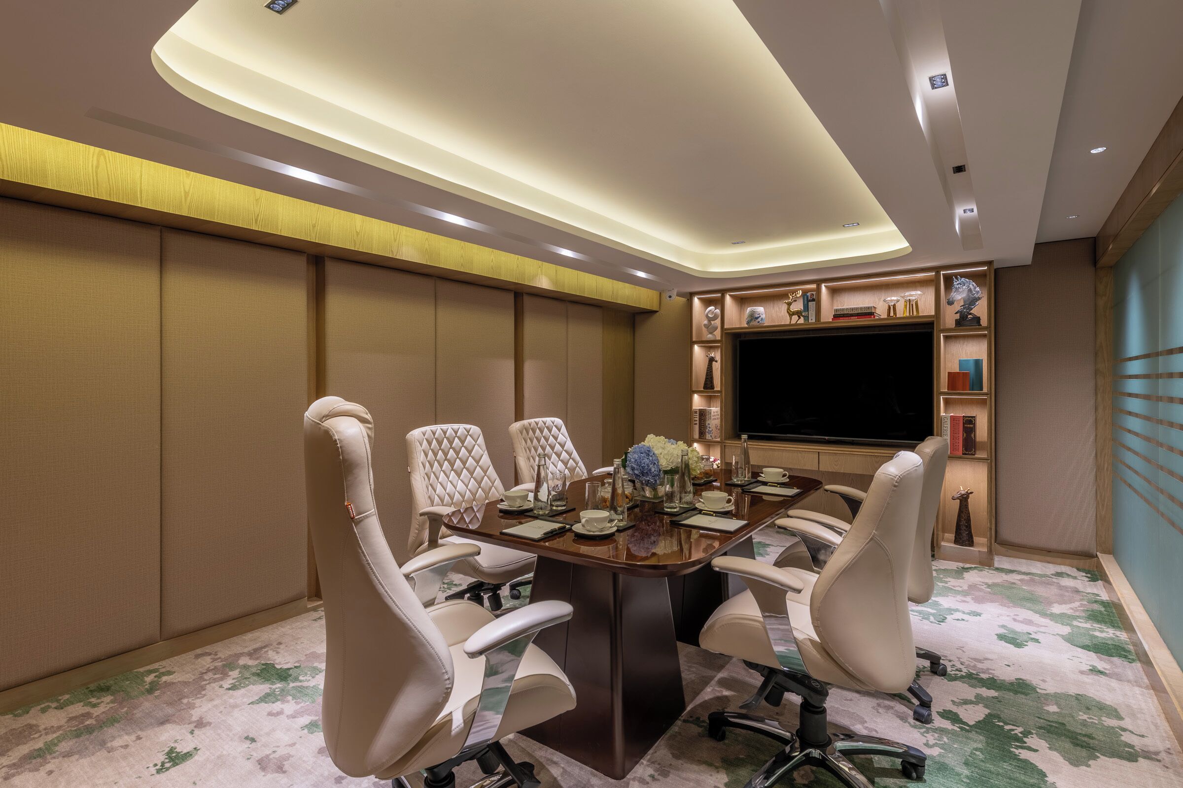 A conference room with a large table, four chairs, a flat-screen TV, and decorative items on shelves.