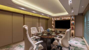 A conference room with a large table, four chairs, a flat-screen TV, and decorative items on shelves.