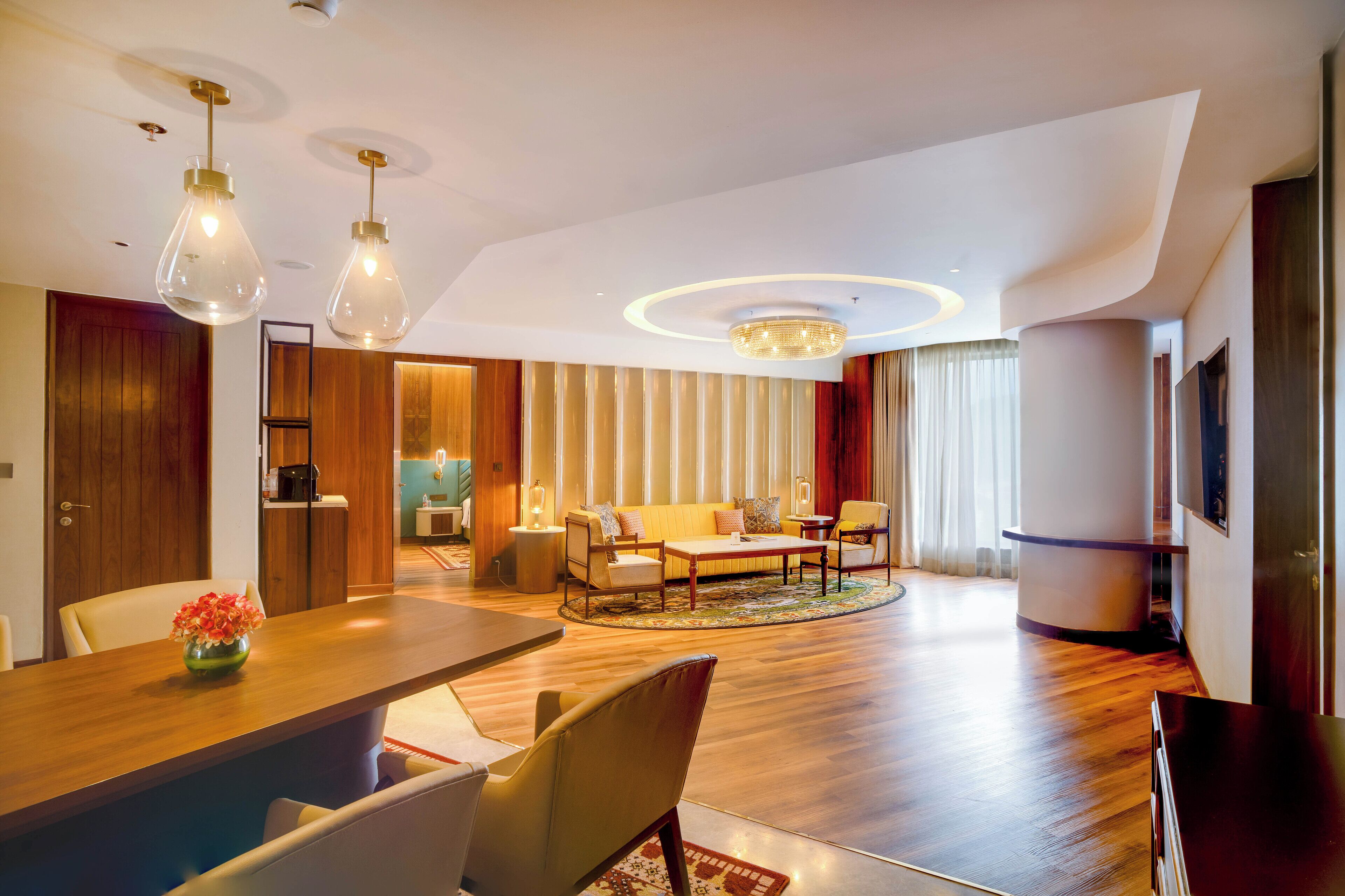 A modern living room with a wooden floor, a round coffee table, a sofa, and a dining area with a wooden table and chairs.