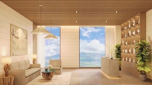 Un moderno hall de hotel con un ventanal grande que ofrece vistas al océano, un mostrador de recepción y una pared con jarrones decorativos.