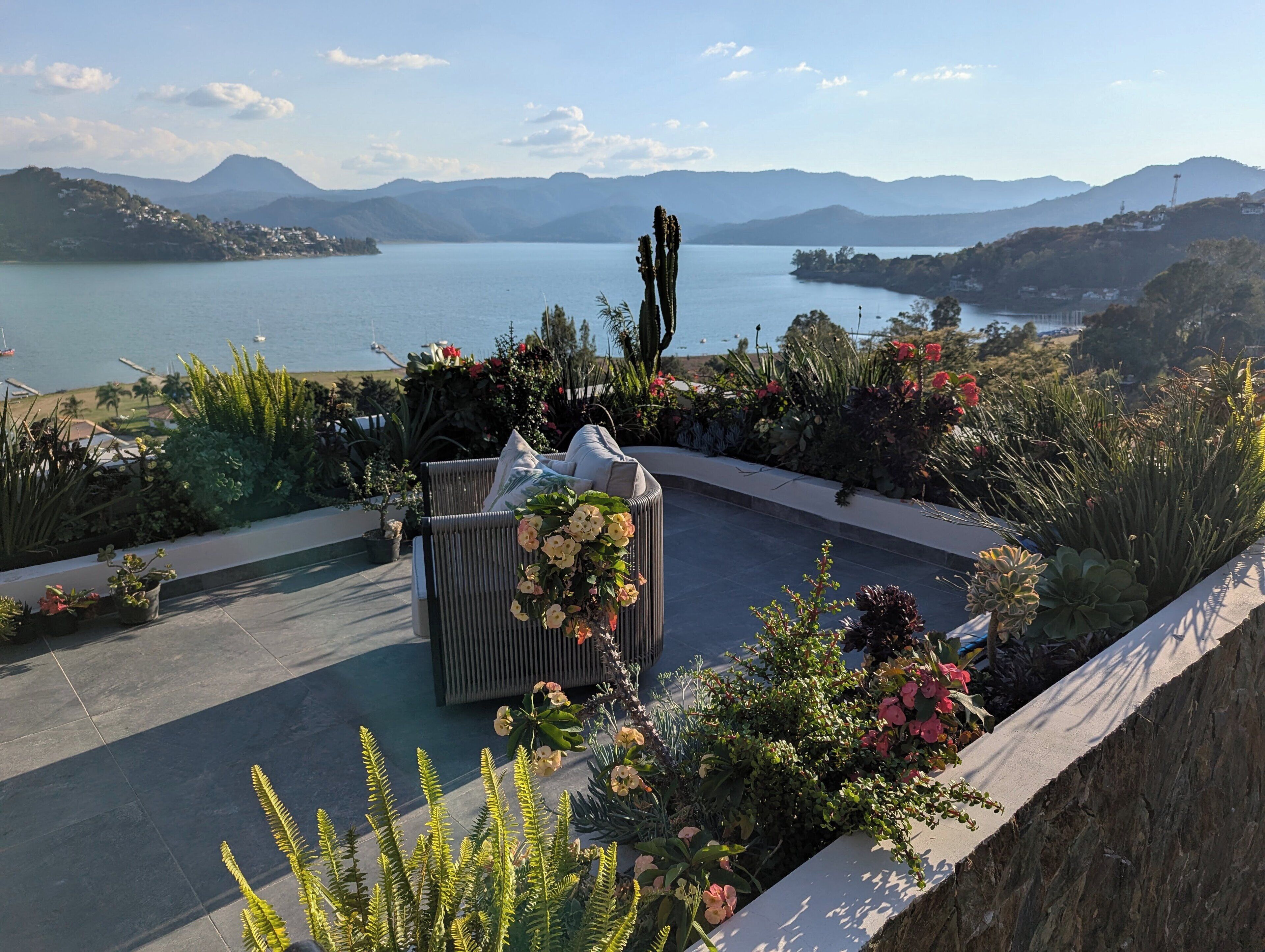 Een terras met een zithoek, een cactus en uitzicht op een meer en bergen.