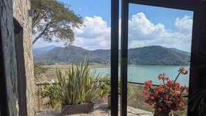 A balcony with a view of a lake and mountains, featuring potted plants and a wooden deck. - Designer House with Spectacular Lake Views, Jacuzzi and Lush Gardens (Valle de Bravo)