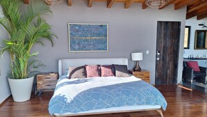 A bedroom with a bed, a large potted plant, a painting on the wall, and a wooden door. - Designer House with Spectacular Lake Views, Jacuzzi and Lush Gardens (Valle de Bravo)