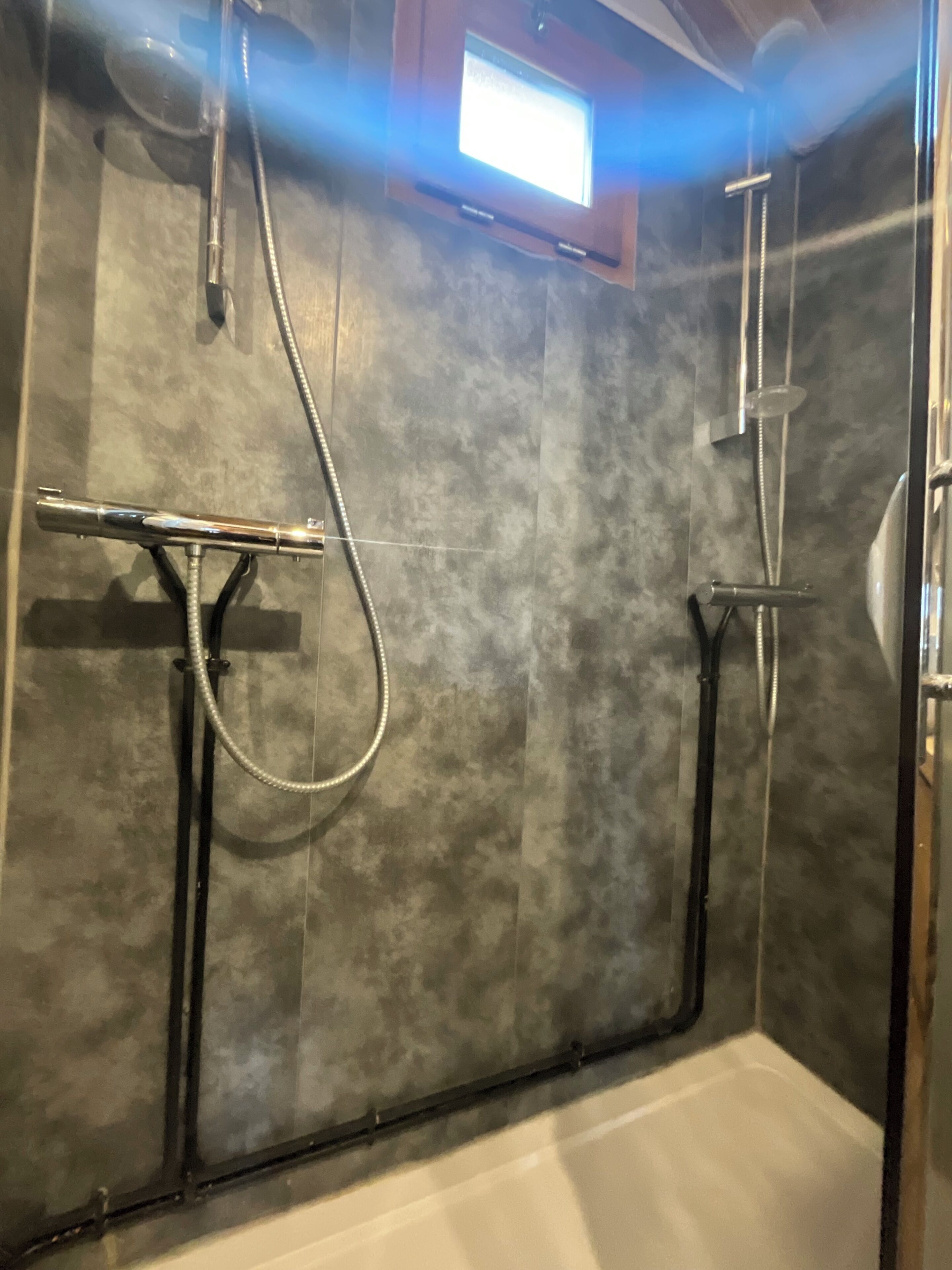 Un espace douche doté d’une porte en verre, d’un pommeau de douche à main et d’un robinet mural.