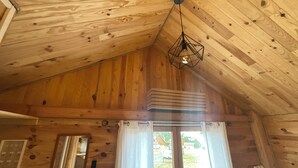 A wooden cabin interior with a sloped ceiling, a hanging light fixture, and a sliding glass door leading outside. - Wooden chalet at the foot of the slopes 4-season ski resort CAMURAC (Camurac)