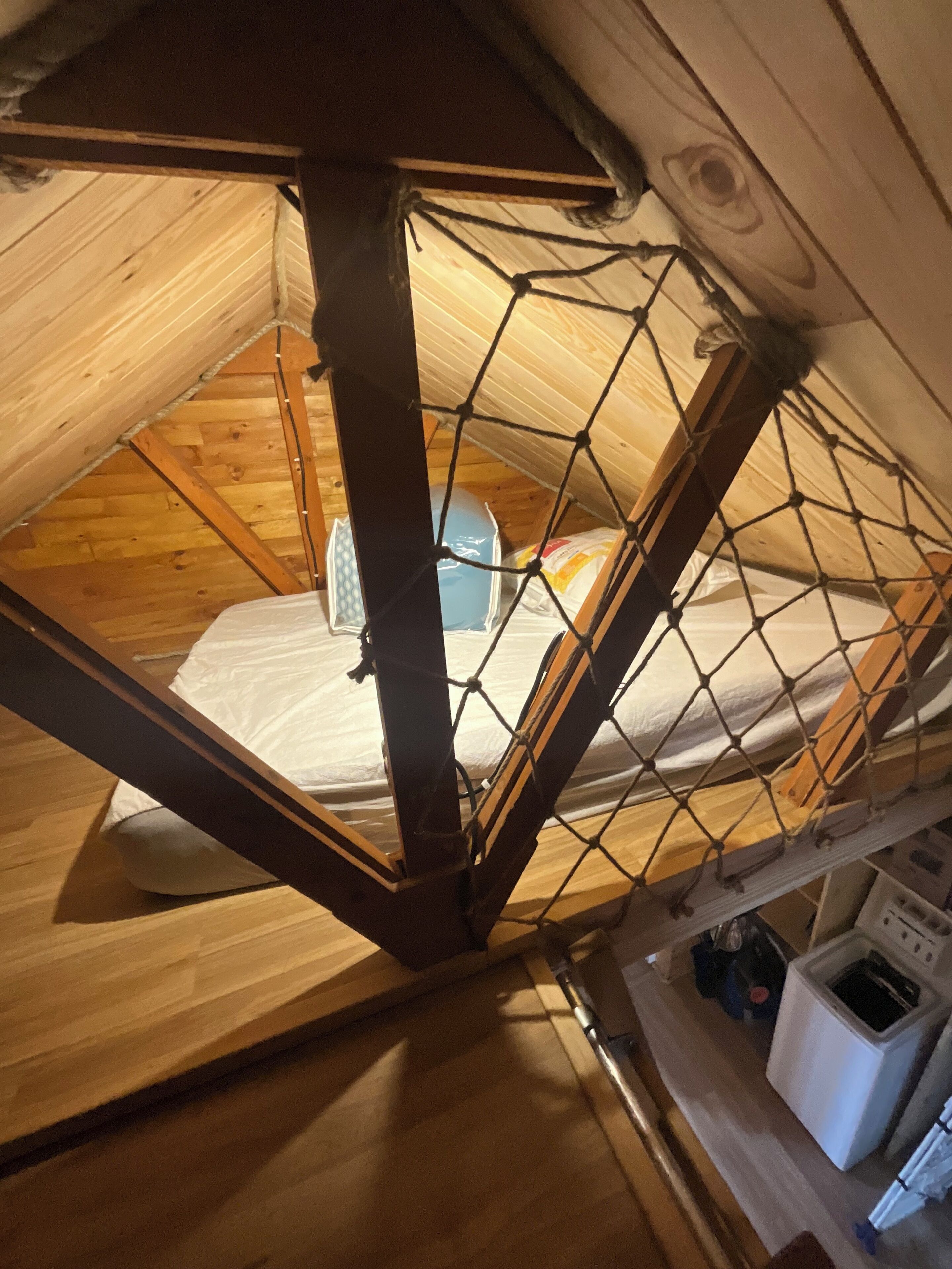Un dormitorio pequeño y cerrado en el ático, con suelo de madera, una cama y una ventana.