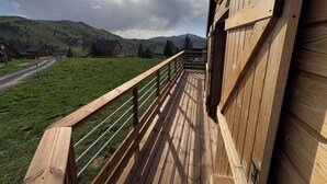 A wooden balcony with a metal railing overlooking a green field and houses in a mountainous area. - Wooden chalet at the foot of the slopes 4-season ski resort CAMURAC (Camurac)