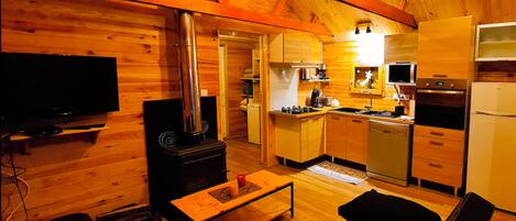 A cozy wooden cabin interior with a TV, a fireplace, a kitchen, and a dining area.