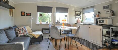 A compact living space with a sofa, dining table, chairs, a kitchenette, and a window with a view of greenery.