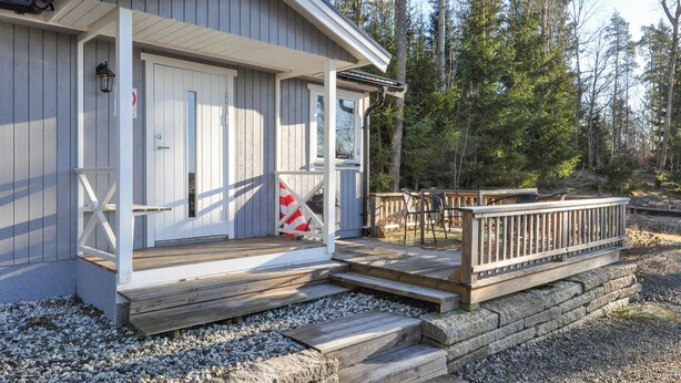 Une cabane dotée d’une terrasse en bois, d’un porche avec des marches et offrant une vue sur une forêt.