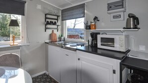 Une cuisine compacte avec des meubles blancs, un four à micro-ondes, une machine à café et une fenêtre donnant sur une maison.