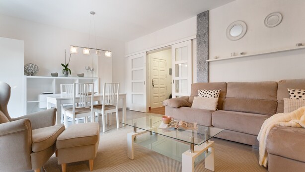 Una sala de estar moderna con una mesa de centro de vidrio, sofá color beige y muebles blancos.