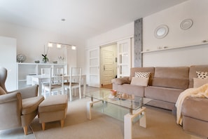 Una sala de estar moderna con una mesa de centro de vidrio, sofá color beige y muebles blancos.