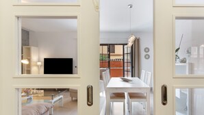 Un interior moderno con comedor, televisor y cocina a la vista a través de un umbral abierto.