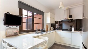 Una cocina moderna con televisión integrada, armarios blancos, un ventanal grande y un comedor con mesa y sillas blancas.