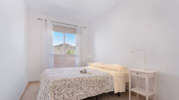 Un dormitorio con cama, mesita de noche, lámpara y ventana con vistas al exterior.