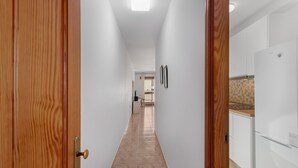 Un corridoio con porte in legno, pareti bianche e un angolo cottura con mobili bianchi e un frigorifero.