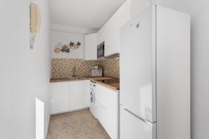A kitchen with white cabinets, a microwave, a washing machine, and a refrigerator.