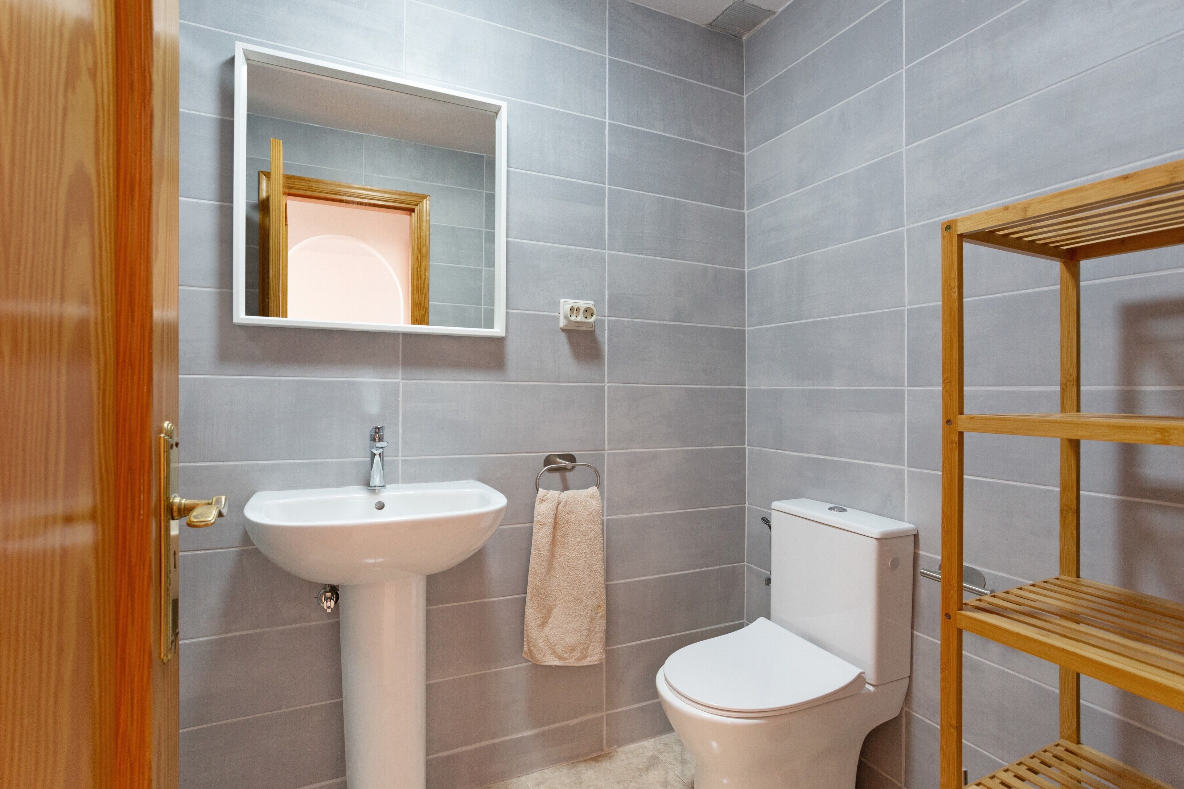 A bathroom with a white sink, a toilet, a wooden shelf, and a mirror.