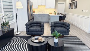 Ein modernes Wohnzimmer mit zwei grauen Sesseln, einem schwarzen Couchtisch, einer Stehlampe und einem Streifen Teppich.