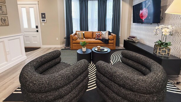 Ein modernes Wohnzimmer mit einem braunen Ledersofa, zwei Sesseln, einem Couchtisch und einem an der Wand befestigten Flachbildfernseher.