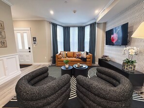 Ein modernes Wohnzimmer mit einem braunen Ledersofa, zwei Sesseln, einem Couchtisch und einem an der Wand befestigten Flachbildfernseher.