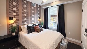 Ein modernes Schlafzimmer mit einem großen Bett, einem Deckenventilator, einer Wandleuchte und einem mit Vorhängen versehenen Fenster.