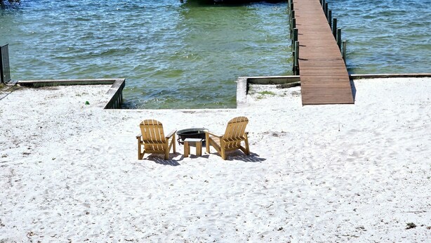 A wooden dock extending into calm water, a covered structure at the dock's end, and two Adirondack chairs on a sandy beach. - Bear Point Bay Front Beach House! Sleeps 12 (Orange Beach)