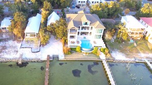 An aerial view of a residential area with a large house featuring a swimming pool, dock, and docked boats. - Bear Point Bay Front Beach House! Sleeps 12 (Orange Beach)
