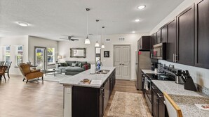 A modern kitchen with dark cabinets, a large island, and a dining area with a sofa and chairs.