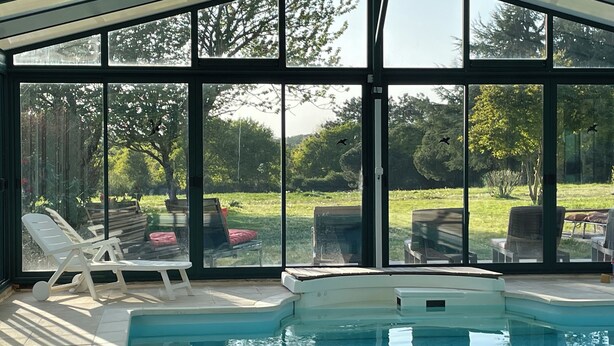 A pool area with lounge chairs and a view of a garden through large windows. - Romantic mini villa - heated pool and wooded park -Les Hauts de Locmiquel (Baden)