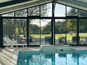 A pool area with lounge chairs and a view of a garden through large windows. - Romantic mini villa - heated pool and wooded park -Les Hauts de Locmiquel (Baden)