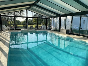 Une piscine intérieure, dotée de parois en verre transparent, entourée de chaises longues et offrant une vue sur l’extérieur.