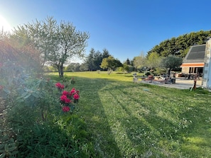 Un jardin bien entretenu, agrémenté d’une terrasse, un bâtiment en pierre doté d’un toit en pente, ainsi qu’une variété d’arbres et d’arbustes.