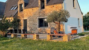A stone house with a sloped roof, a small garden with outdoor seating, and a tree. - Romantic mini villa - heated pool and wooded park -Les Hauts de Locmiquel (Baden)