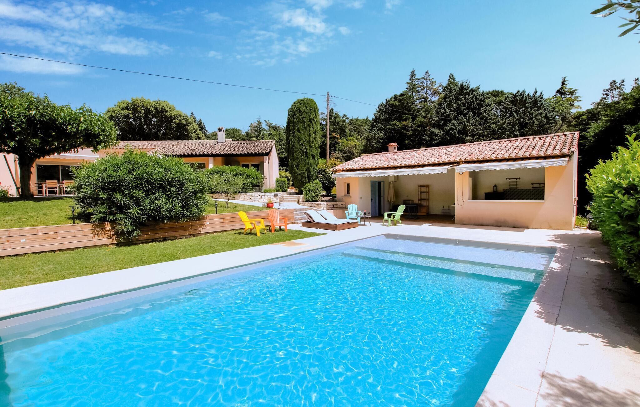 A swimming pool with a tiled deck, surrounded by a well-maintained lawn and a small building with a tiled roof.