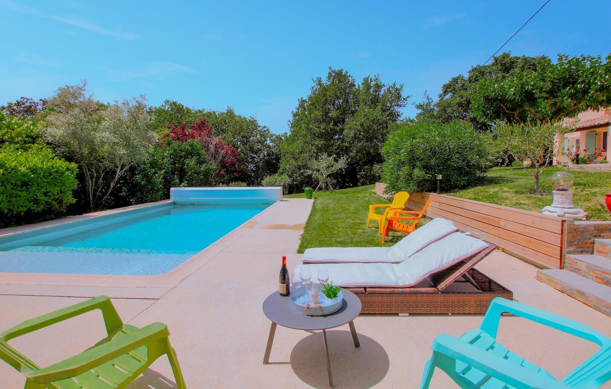 Piscina com espreguiçadeiras e uma mesa, rodeada por vegetação e um deck de madeira.