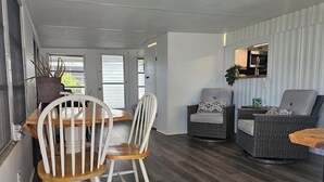 A modern interior with a dining area, two wicker chairs, a wooden table, and a kitchen area with a refrigerator and microwave. - Slice of Paradise w/community pool near beaches & downtown! (Fort Myers)