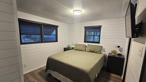A bedroom with a bed, two nightstands, a TV mounted on the wall, and two windows with blinds. - Slice of Paradise w/community pool near beaches & downtown! (Fort Myers)