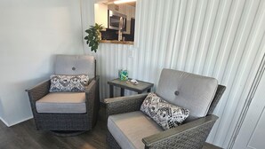 Two wicker armchairs with cushions, a small table, and a potted plant in a room with a wooden floor and a white wall. - Slice of Paradise w/community pool near beaches & downtown! (Fort Myers)